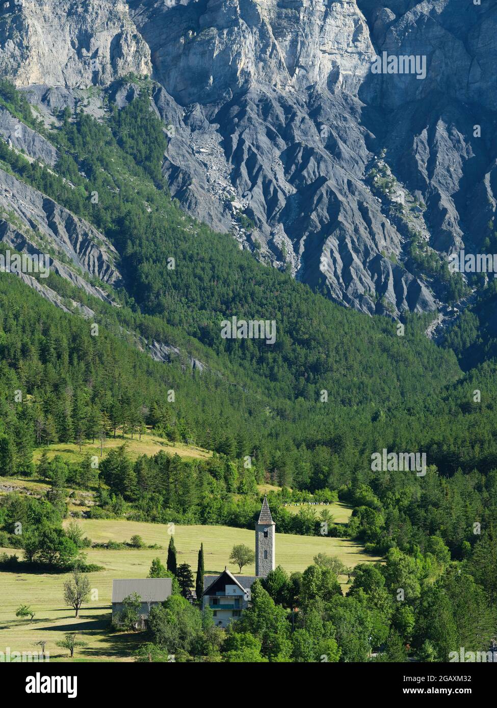 AERIAL VIEW. Church of Villeneuve d'Entraunes standing at the foot of a large rock face. Upper Var Valley, Alpes-Maritimes, France. Stock Photo