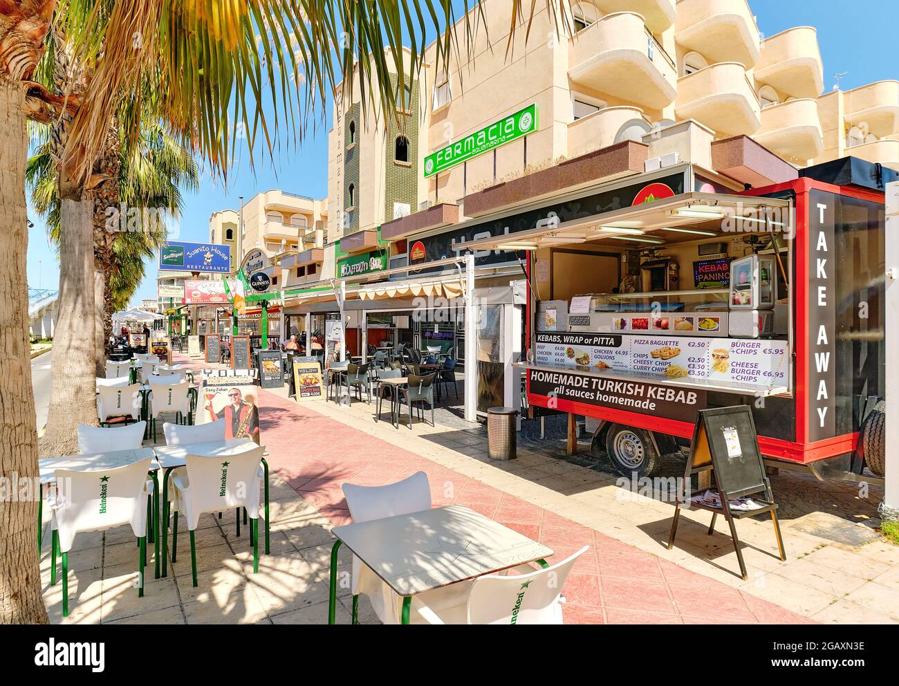 Orihuela, Spain - May 14, 2021: Commercial street with outdoor restaurants and cafes in the street palm lined street of Cabo Roig. Tourism and travel, Stock Photo