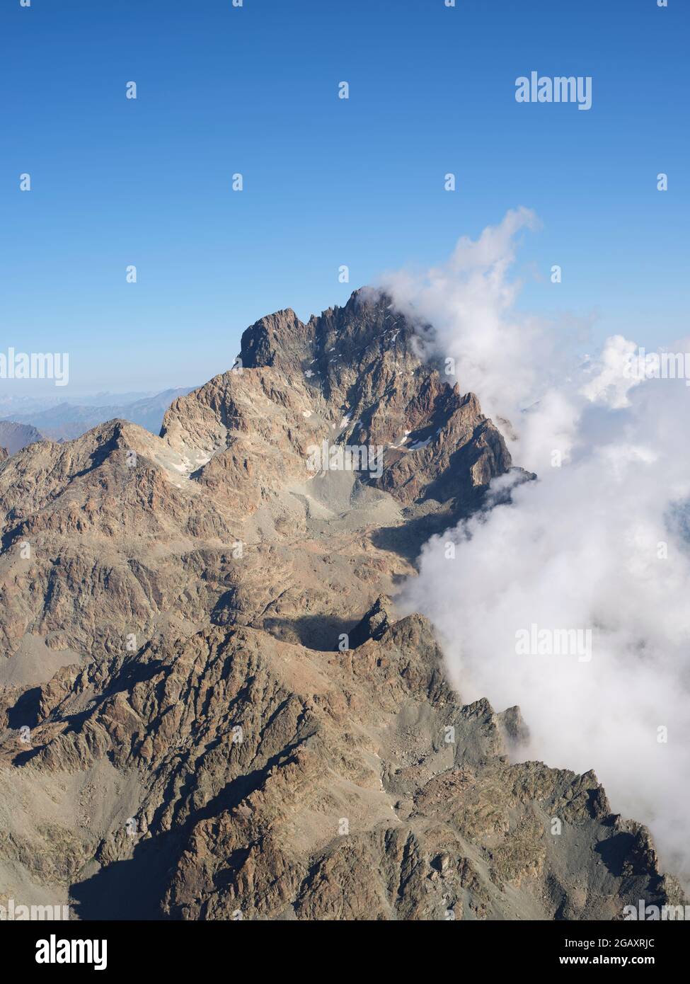 AERIAL VIEW. Southern craggy rock face of Monte Viso (3841m) with clouds to the east above the Po Plain. Province of Cuneo, Piedmont, Italy. Stock Photo