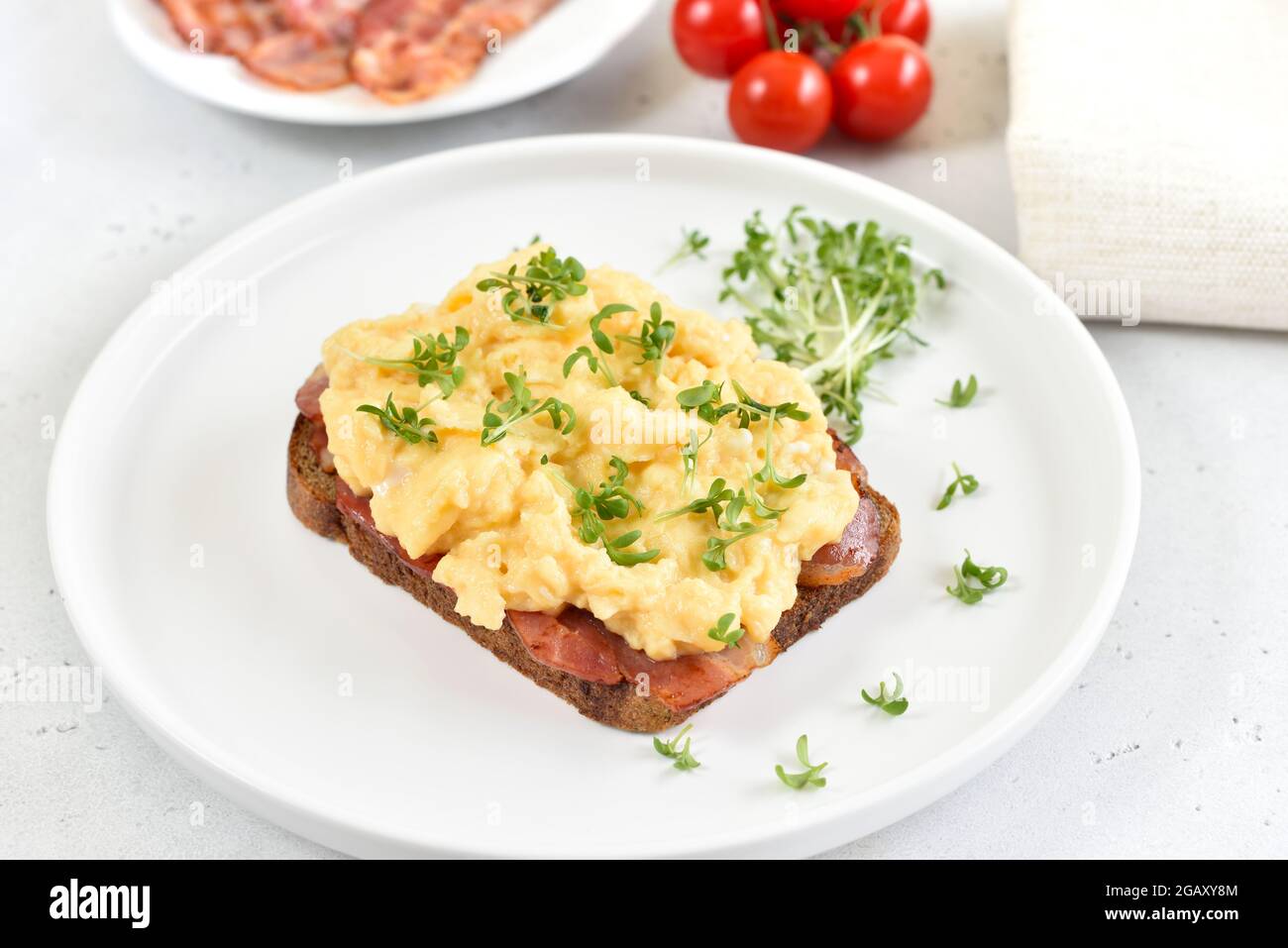 Scrambled eggs with microgreen and bacon on bread, close up Stock Photo