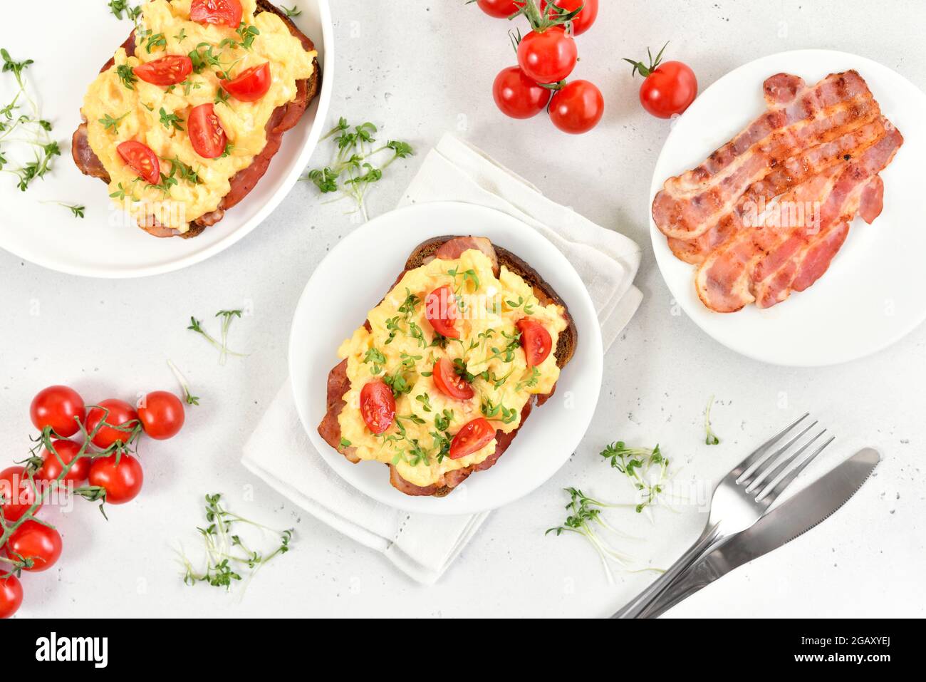 Scrambled eggs with microgreen, bacon and tomatoes on bread. Top view, flat lay Stock Photo
