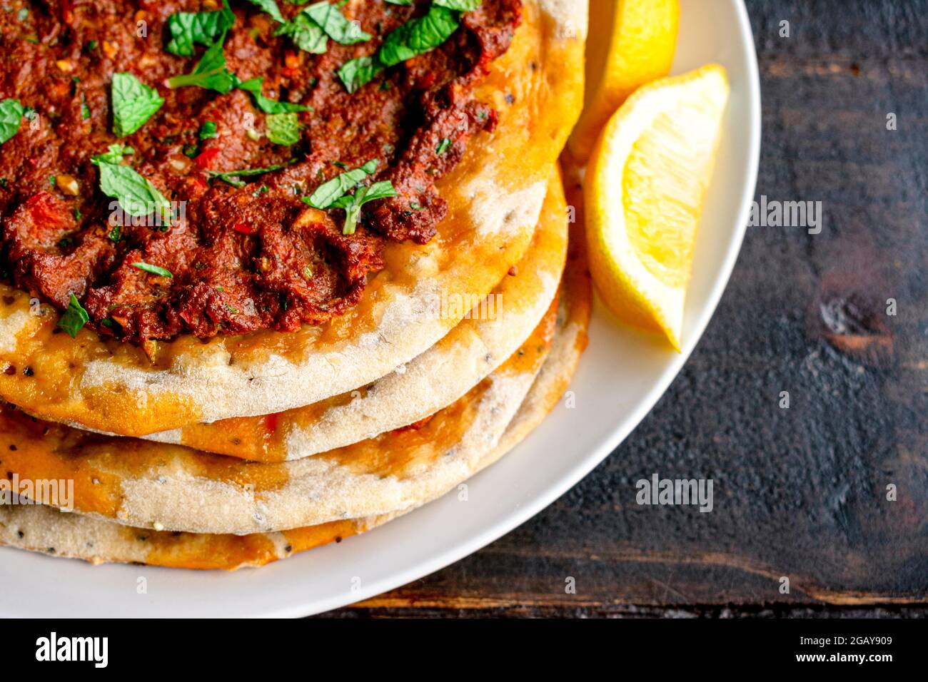 Closeup View of Turkish Lahmacun Served with Lemon Wedges: Turkish flatbreads topped with spiced ground meat and garnished with chopped mint leaves Stock Photo