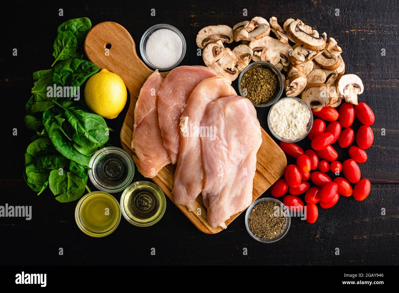 Italian Skillet Chicken with Tomatoes and Mushrooms Ingredients: Raw chicken cutlets, mushrooms, grape tomatoes, and other ingredients for a rustic It Stock Photo