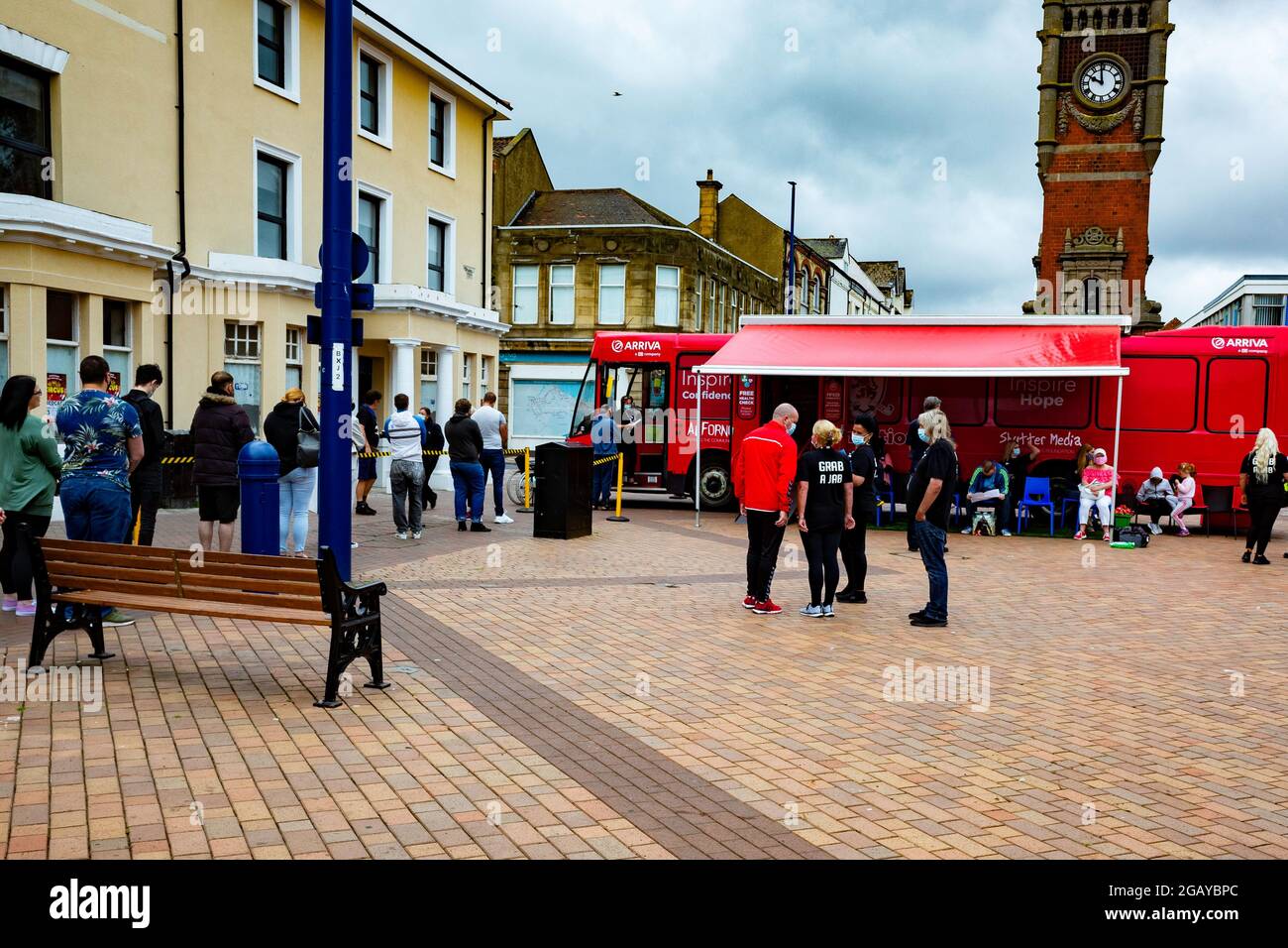 A queue of people awaiting Covid 19 vaccinations at a temporary facility in a red bus at Redcar cleveland helpers wearing tops with Grab a jab on the Stock Photo