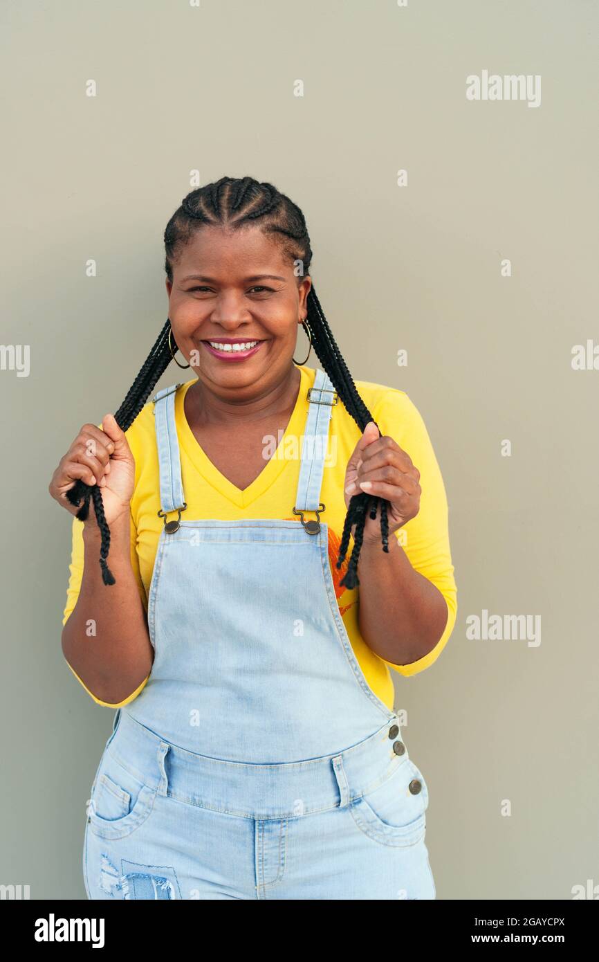 African woman with long hair and braids standing on a gray wall - happiness Stock Photo