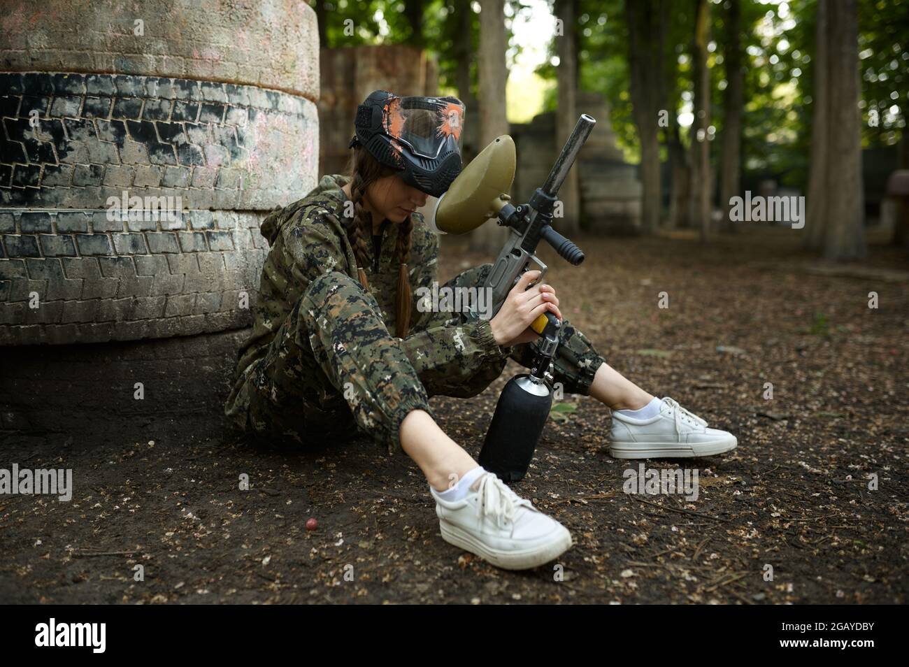 Female paintball player sitting on the ground Stock Photo