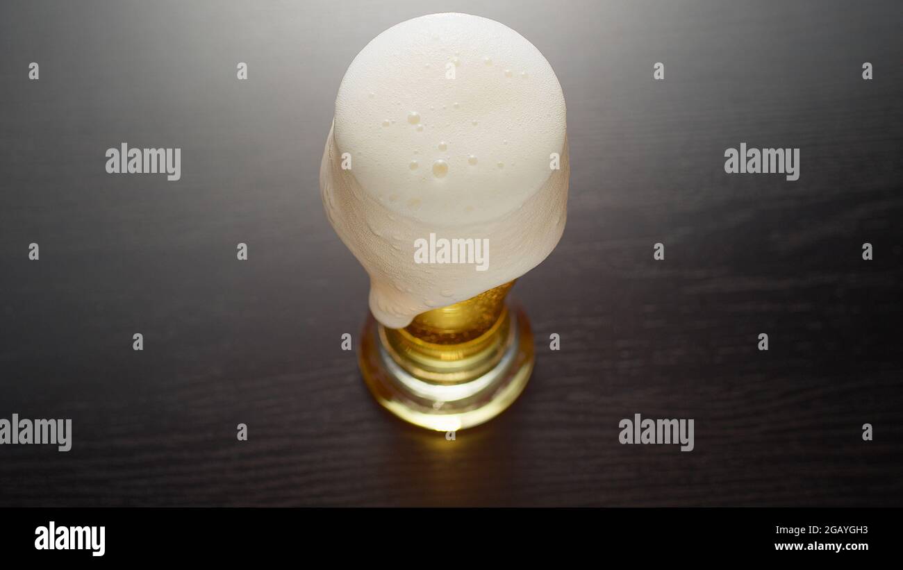 Beer in glass overflowed. Half pint of frothy fresh lager beer on table. Foam goes over the edge. Top view. Stock Photo