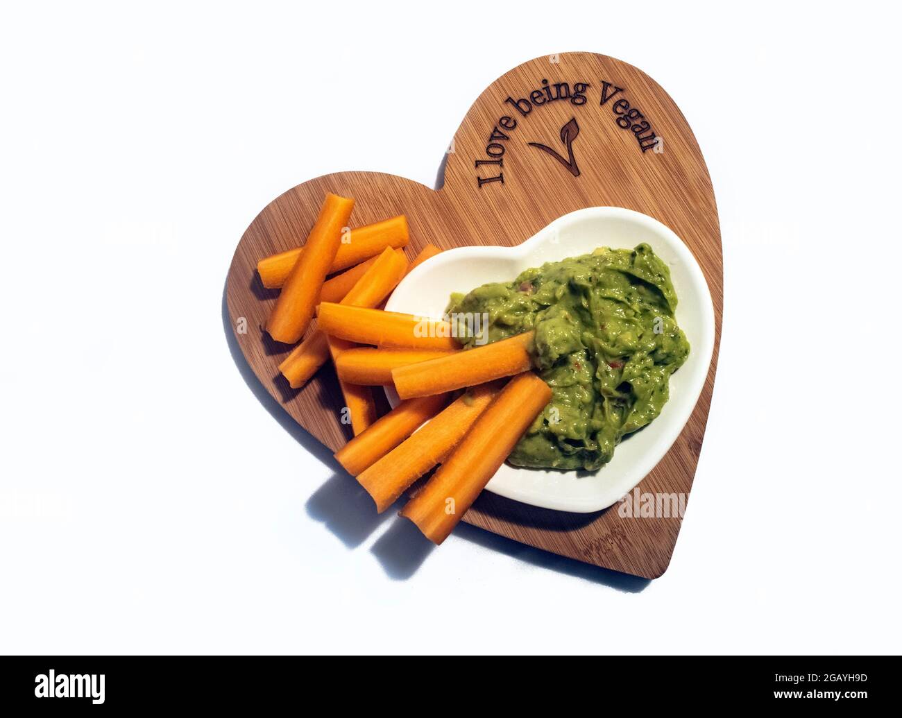 Healthy Vegan Snacking Food - Vegan Quacamole and carrot batons on an 'I Love Being Vegan' Heart-shaped chopping board. Stock Photo