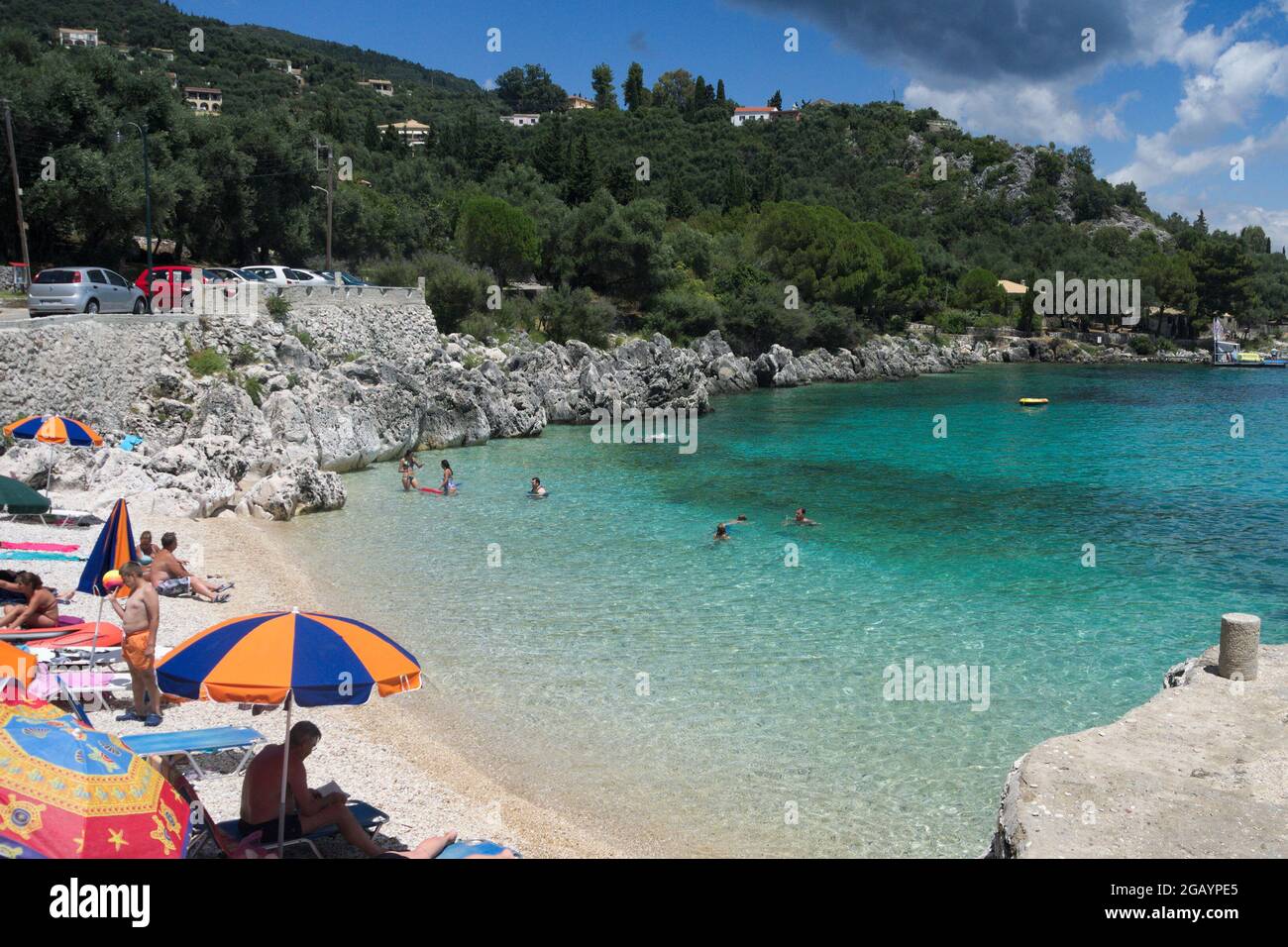 Nissaki, Corfu  Greece  July 10 2014 : Colorful beach, in a beautiful small bay with holiday makers relaxing in the summer sun.  North-East coast. Stock Photo