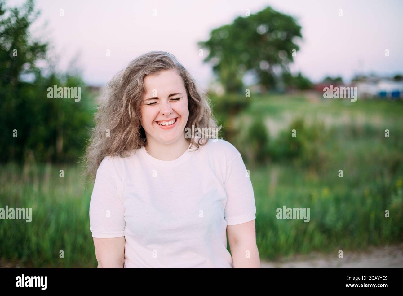 Portrait Of Beautiful Plus Size Young Woman In White Shirt Posing In Summer Field Meadow At Sunset Background Stock Photo