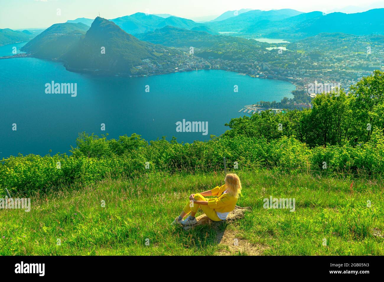 Girl by lakefront of Lugano Lake in Switzerland. Aerial lookout from Monte Bre Mount. Lugano cityscape with San Salvatore mount in Ticino canton. Stock Photo
