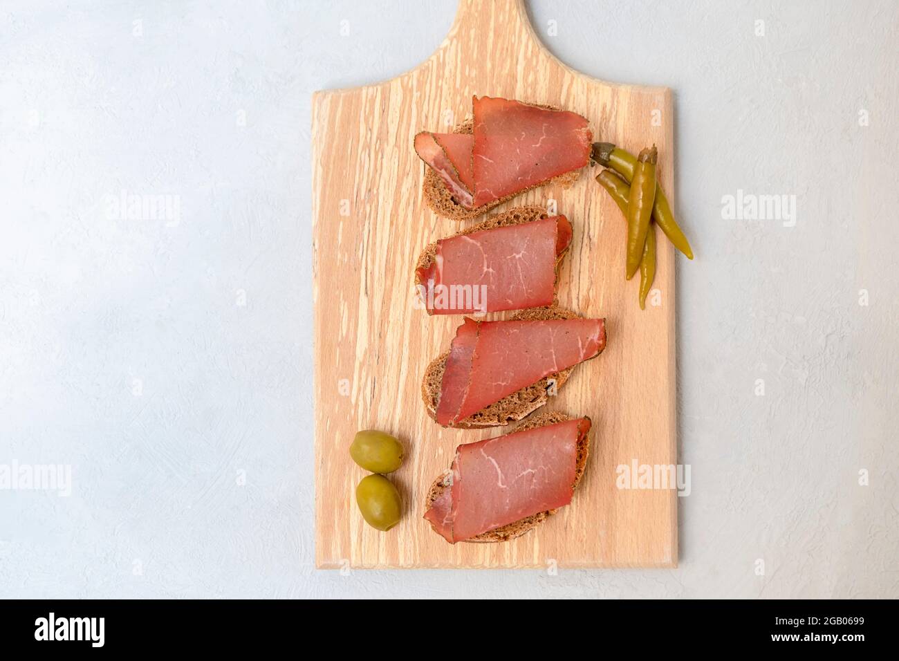 Top view of sandwiches with sliced dried meat served on cutting board on neutral grey background Stock Photo
