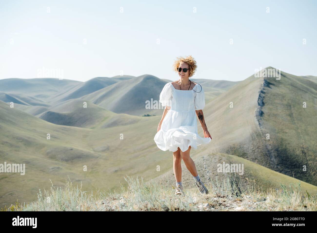 Giggly woman with curly hair and white dress blowing in the wind ...