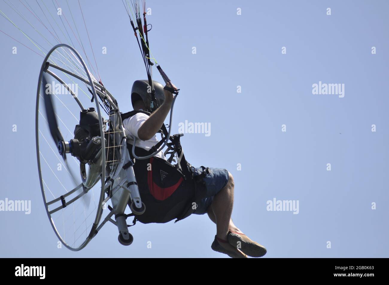 Para glider with a propeller on his back flying over blue water with