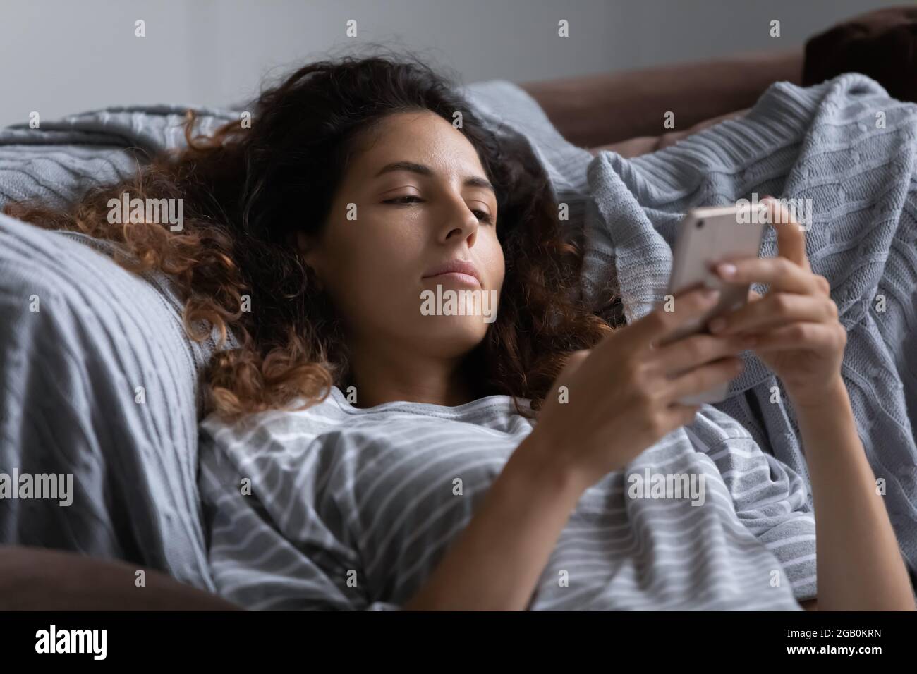Lazy indifferent woman resting in bed, using smartphone Stock Photo