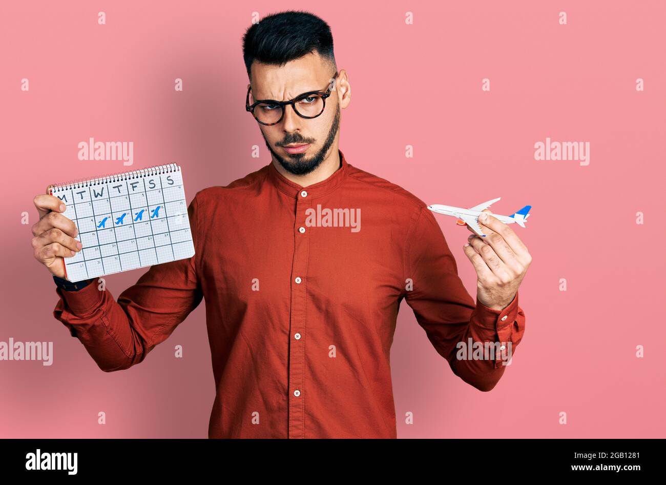 Young hispanic man with beard holding plane toy and travel calendar skeptic and nervous, frowning upset because of problem. negative person. Stock Photo