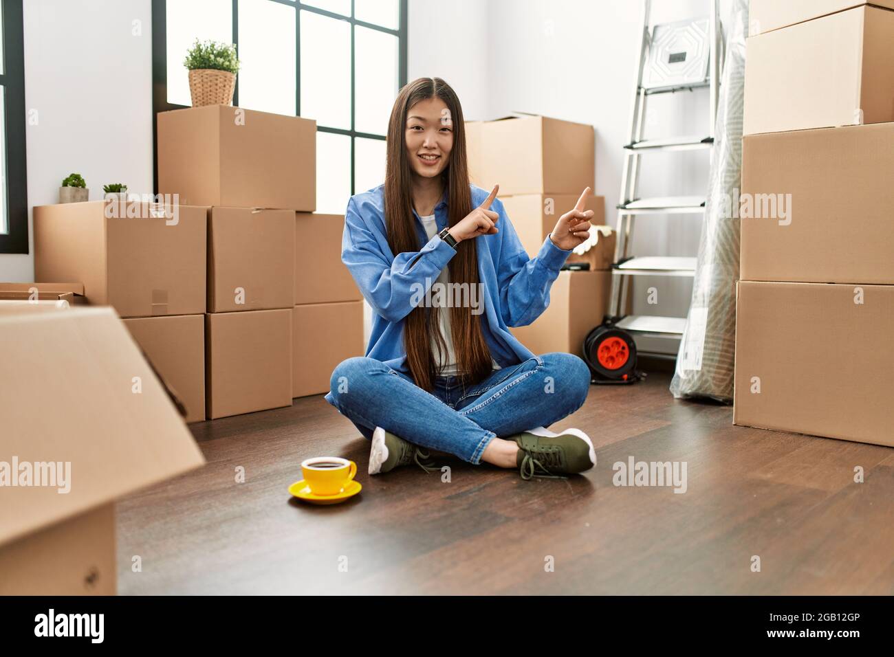 Young chinese girl sitting on the floor at new home smiling and looking ...
