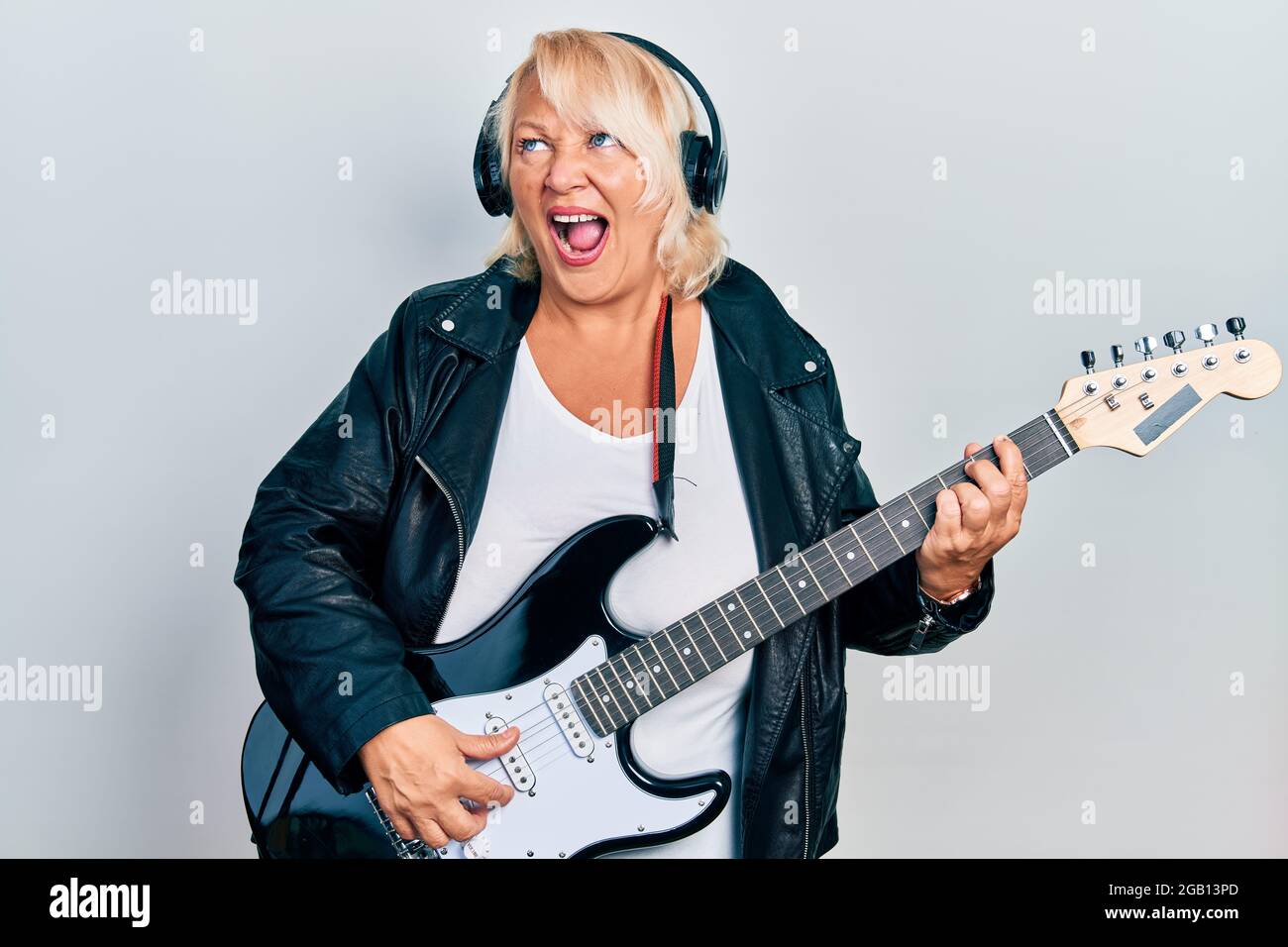 Middle age blonde woman playing electric guitar using headphones