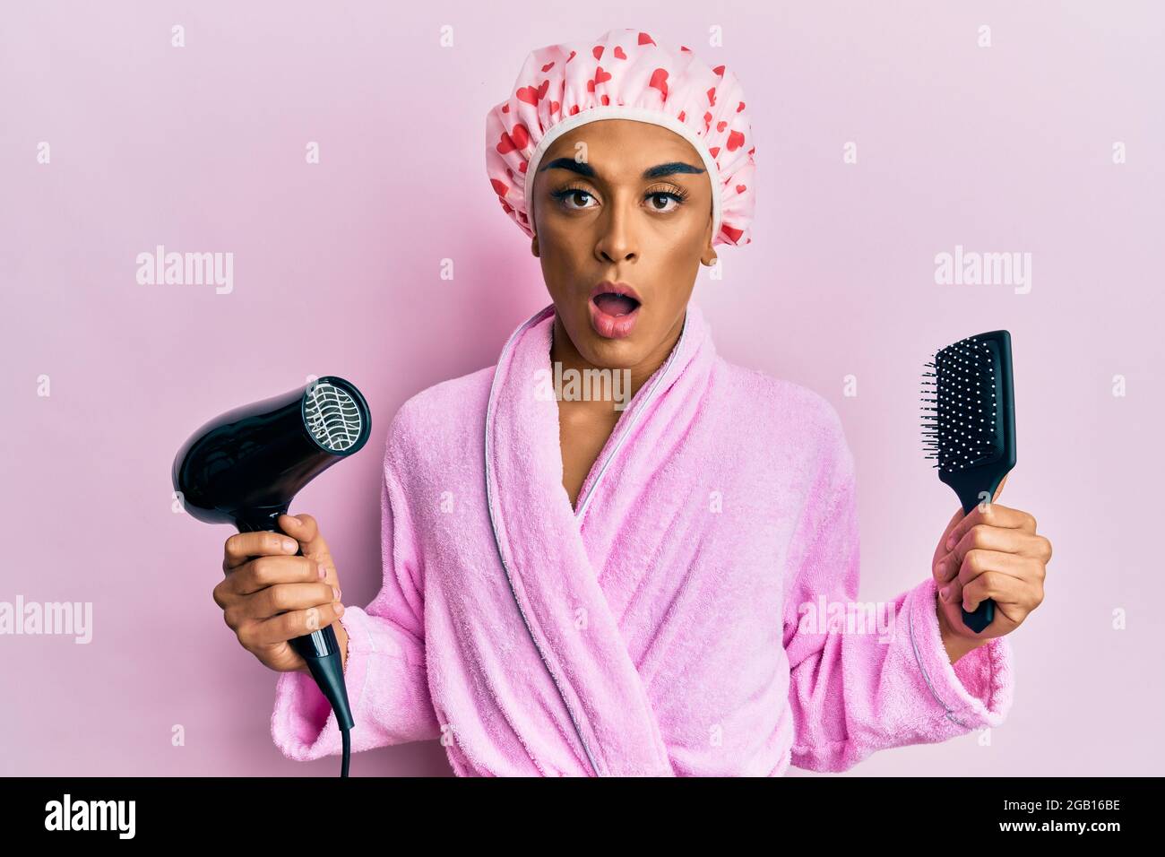 Hispanic man wearing make up wearing shower cap holding hair dryer and ...