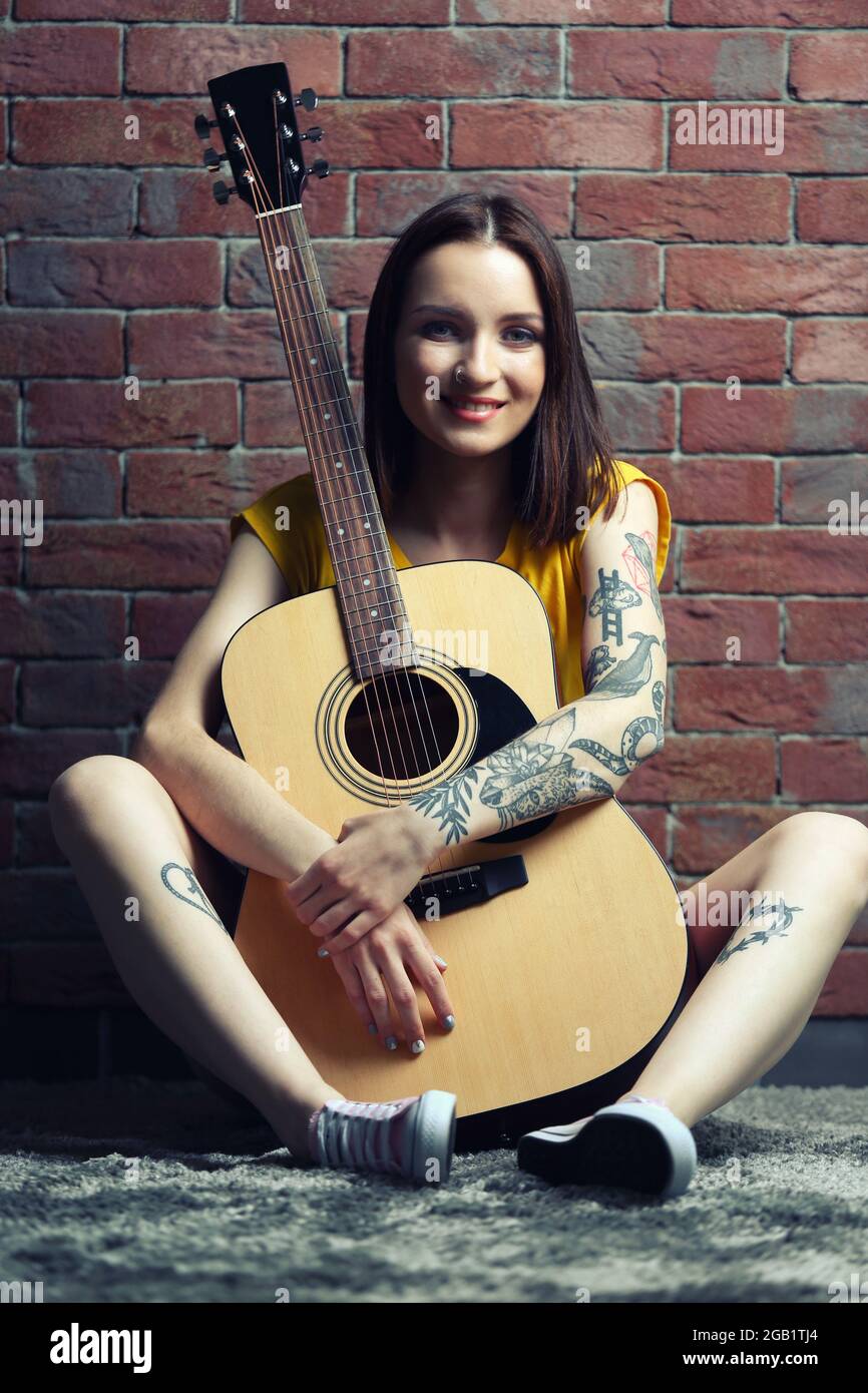 Woman with tattoo playing guitar on brick background Stock Photo - Alamy
