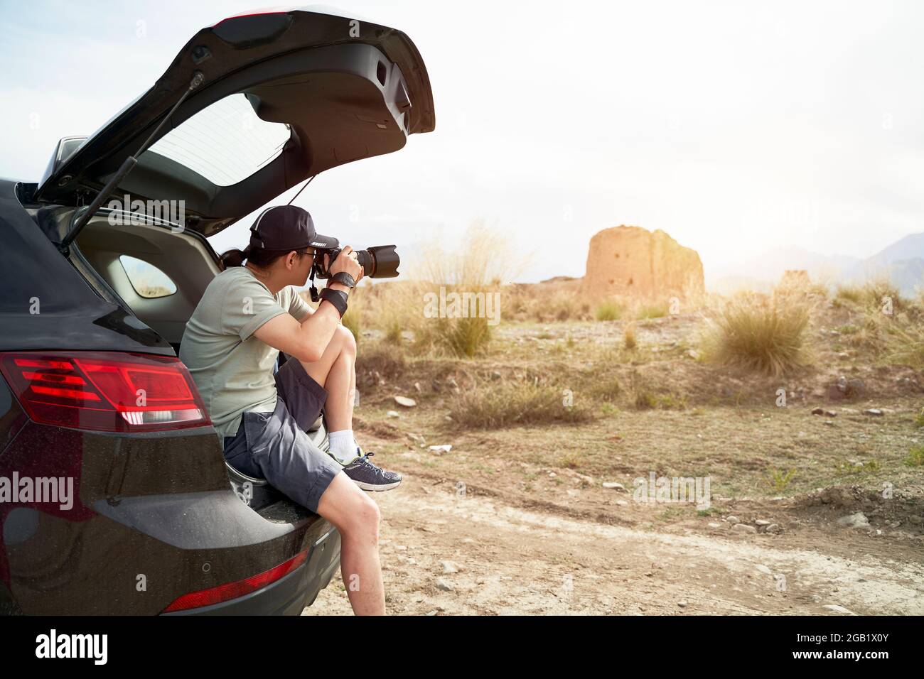 asian photographer sitting at the edge of trunk of a car taking picture of a deserted castle in a historical site Stock Photo