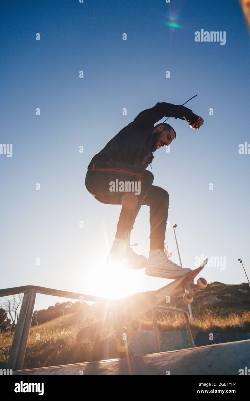 Skateboarder makes jump trick on board against sunset Stock Photo