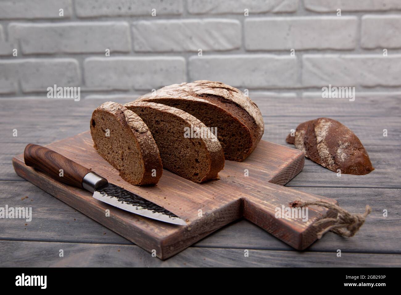 Rye bread round loaf cut into pieces on a wooden board with a knife ...