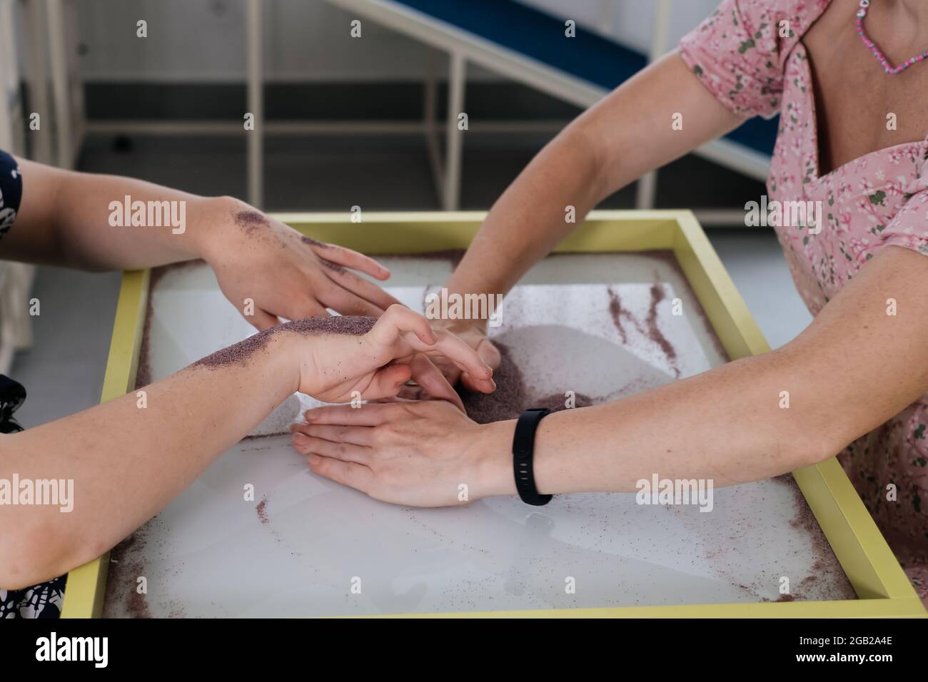 Children with disability getting sensory activity Sand tray, sand table for animation, cerebral palsy boy playing calming game, training fine motor Stock Photo