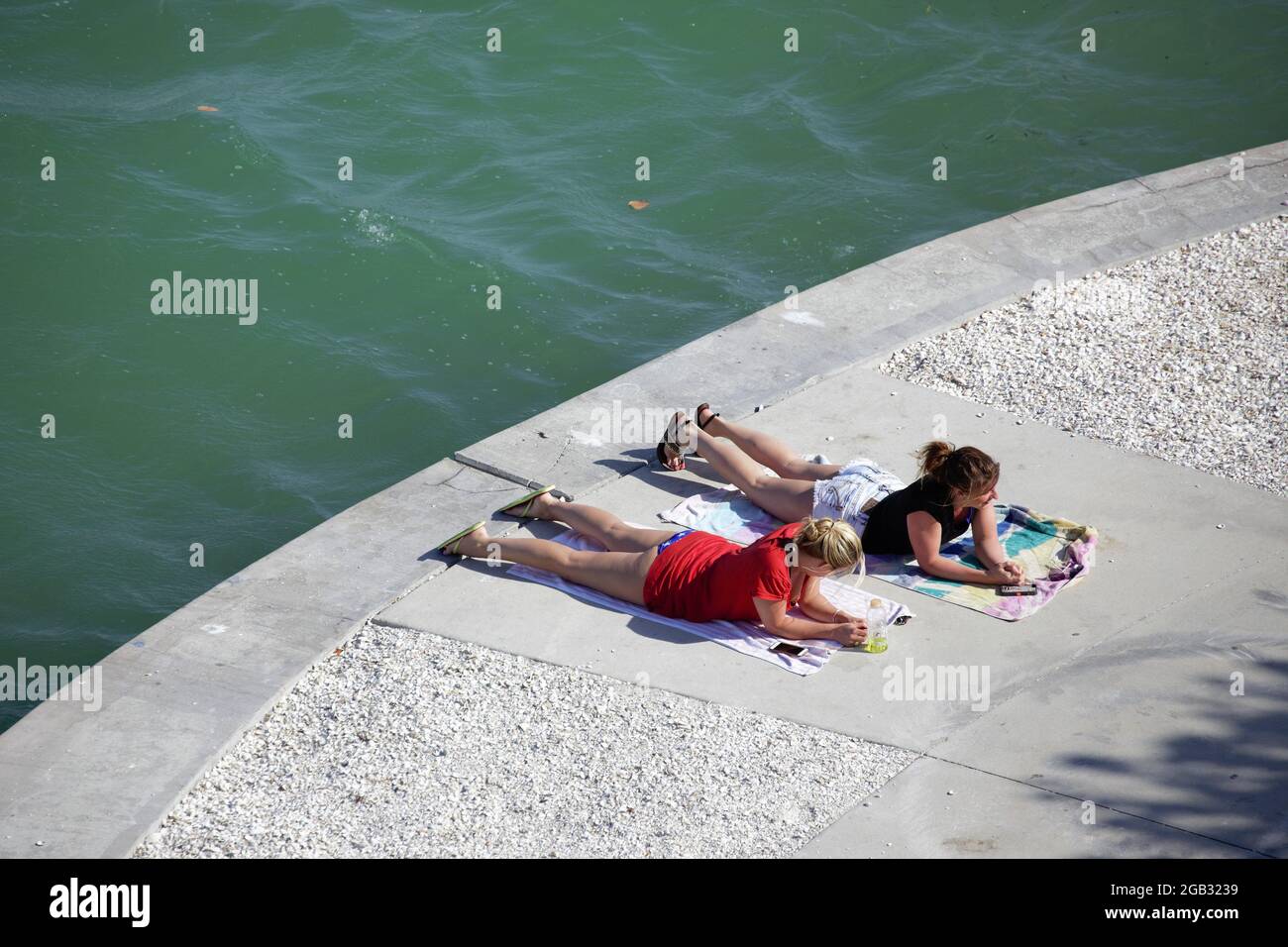 Two young women sunbathing while lying on beach towels near water Stock Photo