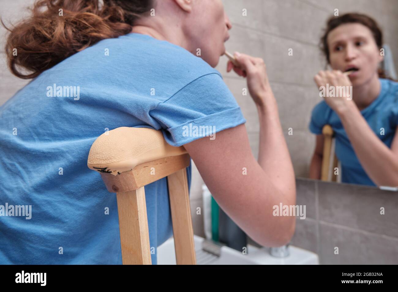 A woman on crutches with a broken leg brushes her teeth in the bathroom