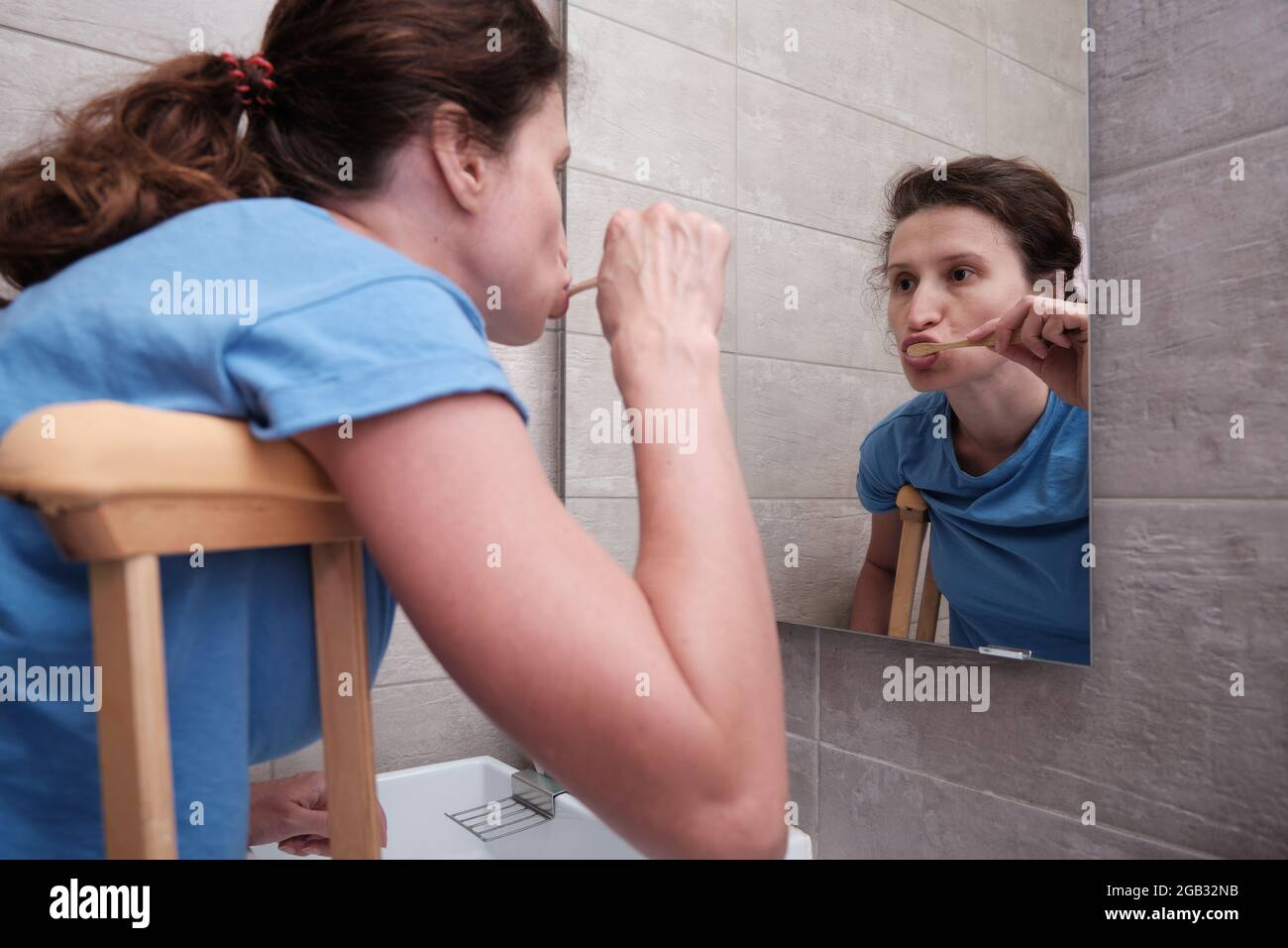 A woman on crutches with a broken leg brushes her teeth in the bathroom