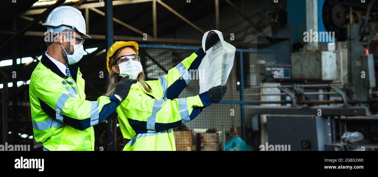 Engineer team wearing face mask, reflective vest and helmet check and control industrial machine  in industry, quality and quality controlling concept Stock Photo
