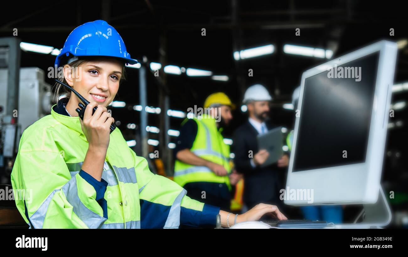 Mechanical engineer woman holding radio working industry wearing safety reflective vest and blue helmet, inspector standing control industrial machine Stock Photo