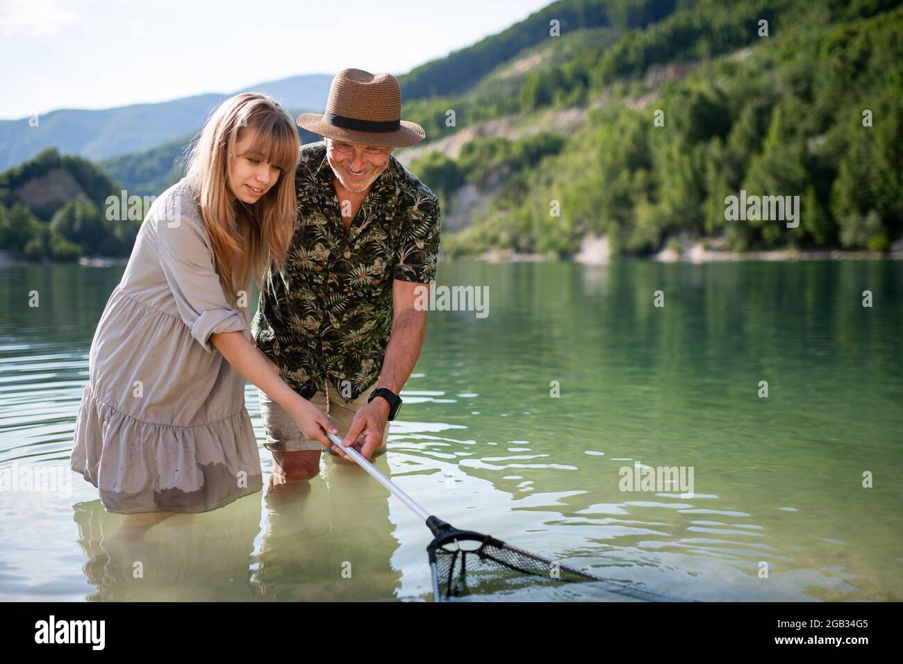 Happy preteen girl and grandfather with fishing net on summer holiday by lake. Stock Photo