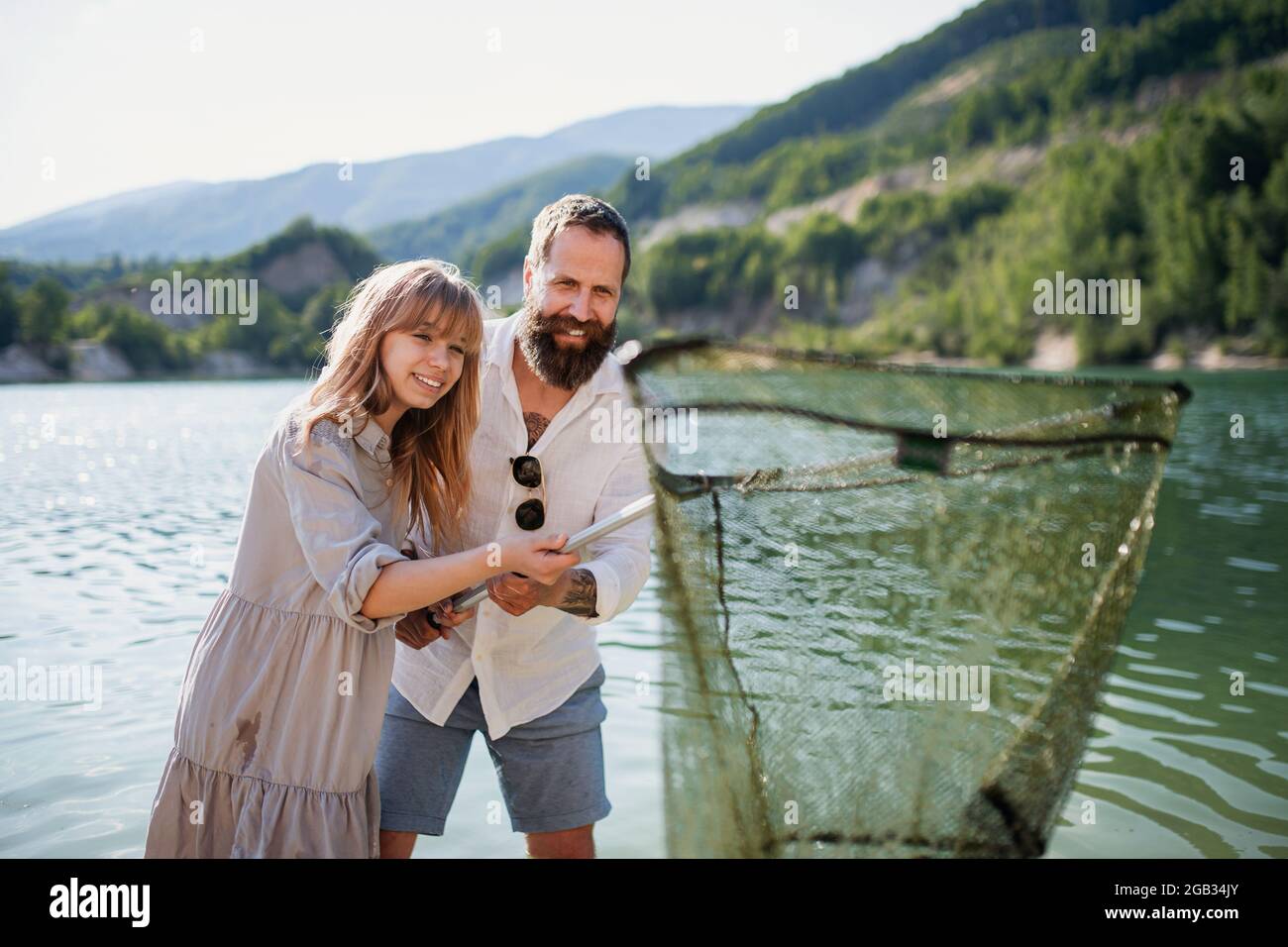 Happy preteen girl and father with fishing net on summer holiday by lake. Stock Photo