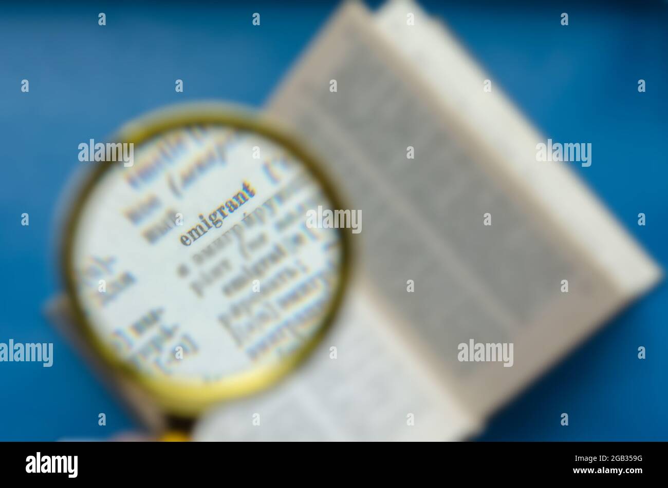 Word Emigrant focus in a magnifying glass. Education, foreign language learning, search for knowledge concept. Defocus, blur, noise effect Stock Photo