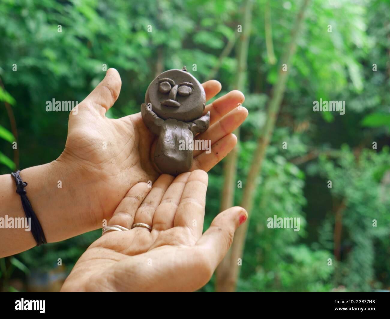 Girl hand holding soil made statue toy sculpture around green natural