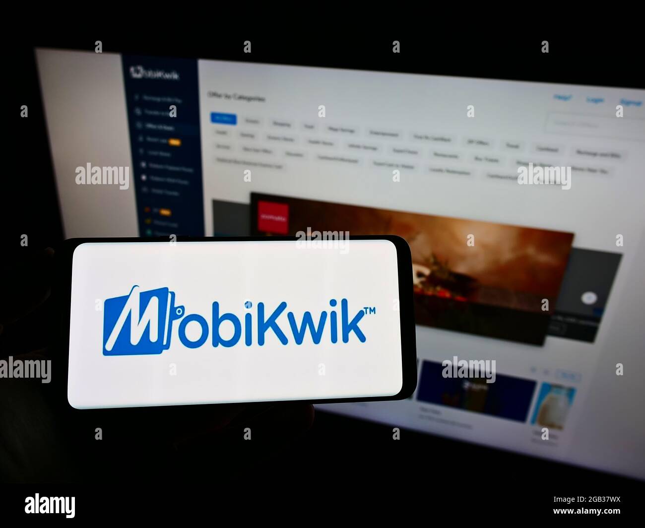Person holding cellphone with logo of Indian financial technology company MobiKwik on screen in front of business web page. Focus on phone display. Stock Photo