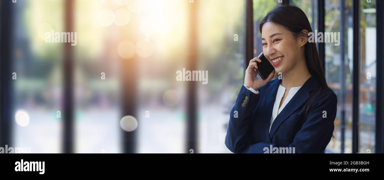 Confidential business Asian young woman cross armed and talk on phone in office, smart and cheerful businesswoman or manager. Stock Photo