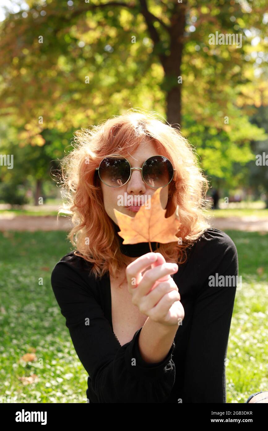 red-haired woman showing an autumn leaf to camera in park Stock Photo