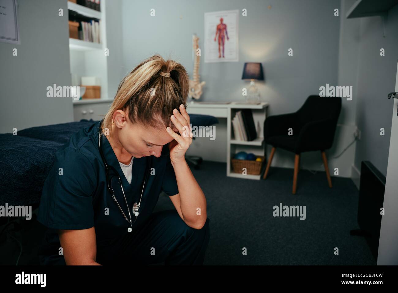 Anxious caucasian female nurse sitting in clinic with headache Stock Photo