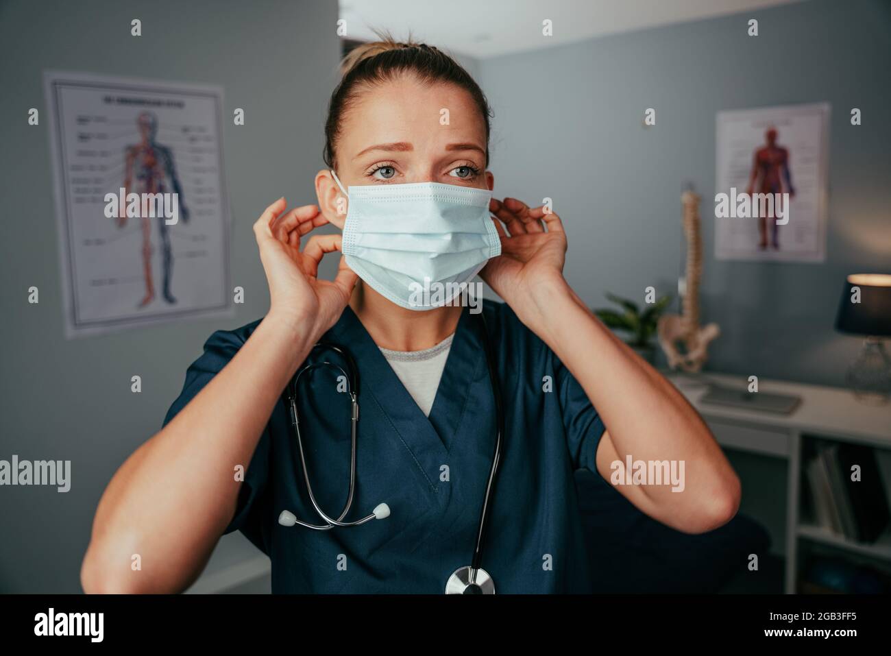 Caucasian female nurse wearing surgical mask standing in doctors clinic Stock Photo