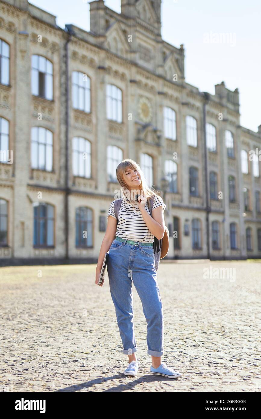 Attractive happy young blonde high school girl or college student with  backpack and laptop wearing jeans standing in university campus.  Educational or studying concept. High quality vertical image Stock Photo -  Alamy