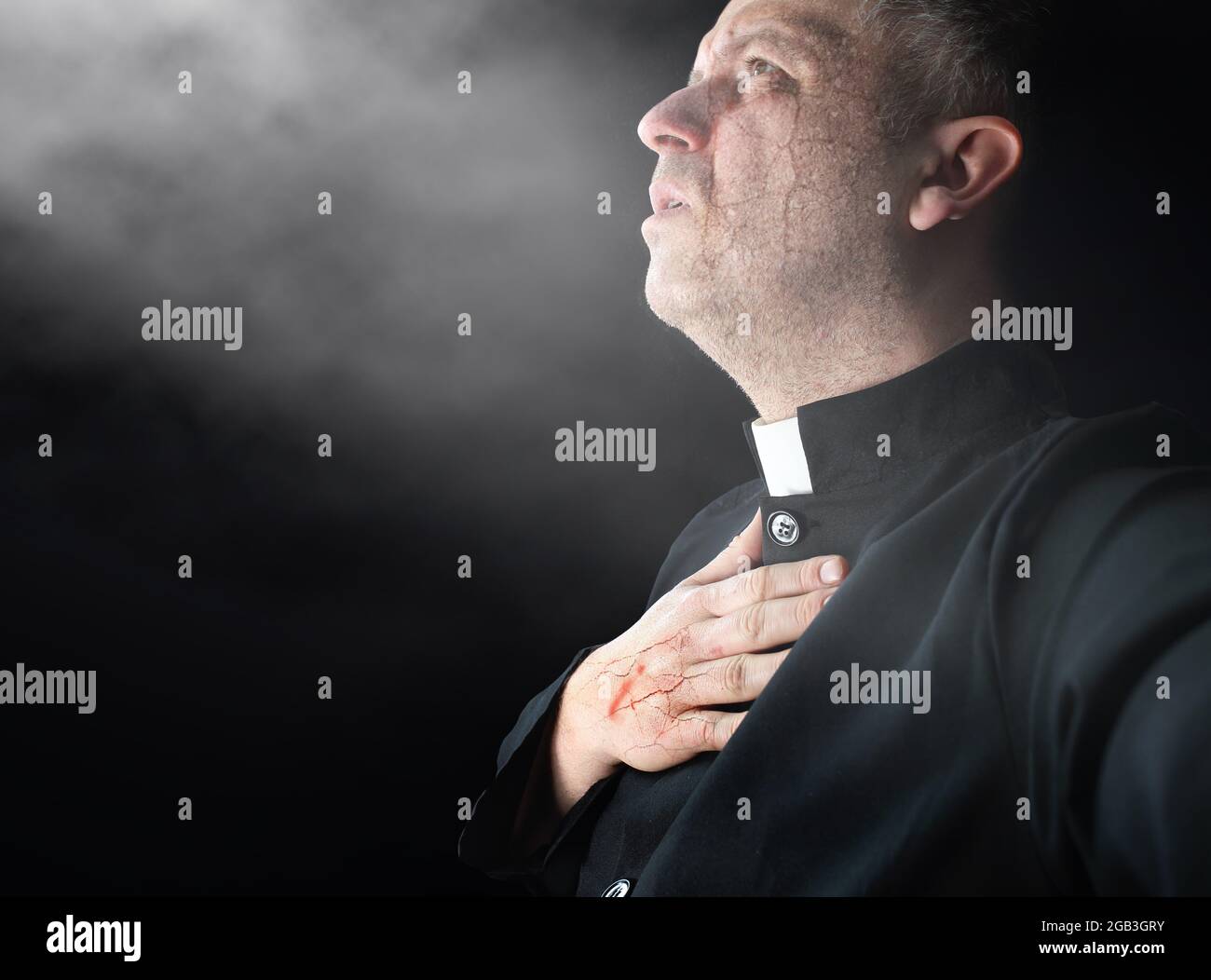 priest prays silently in a dark room Stock Photo