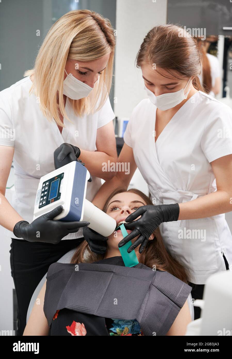 Doctors using portable dental x-ray machine while examining patient teeth in dental office, performing intraoral scanning with modern equipment. Concept of digital dentistry and intraoral radiography. Stock Photo