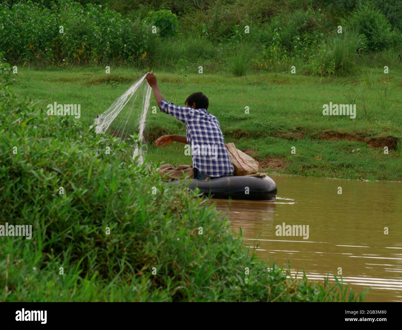 Asian village fisher man catching fishes from filter net at lake side. Stock Photo