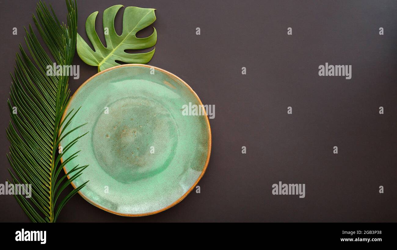 Empty green plate on black background. Luxury dinner plate served with asian kinfolk grunge style tropical palm leaves monstera plant. Mock up empty Stock Photo