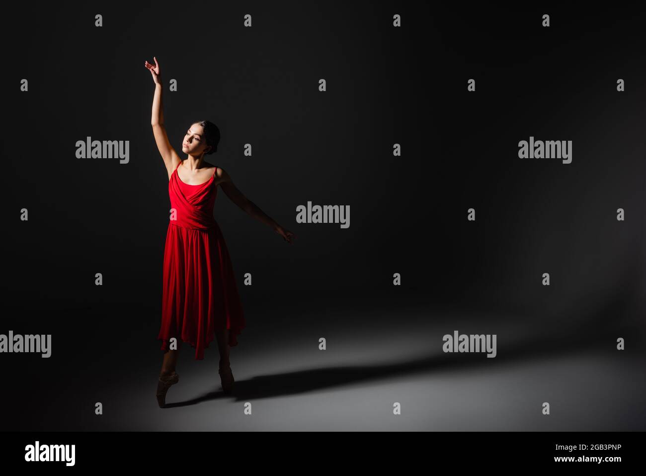 Ballerina in red dress dancing in light on black background Stock Photo ...
