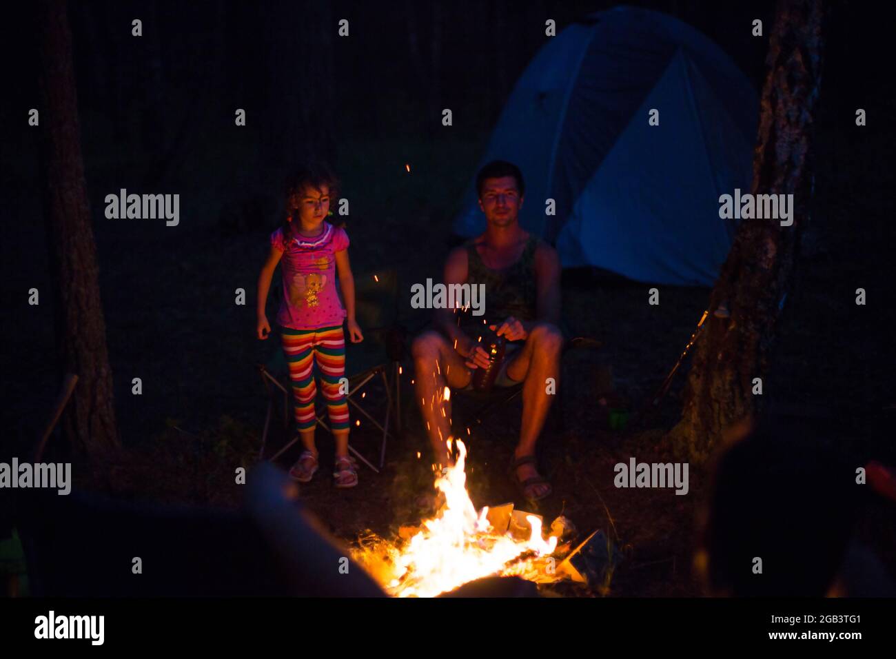 Dad and daughter sit at night by the fire in the open air in the summer