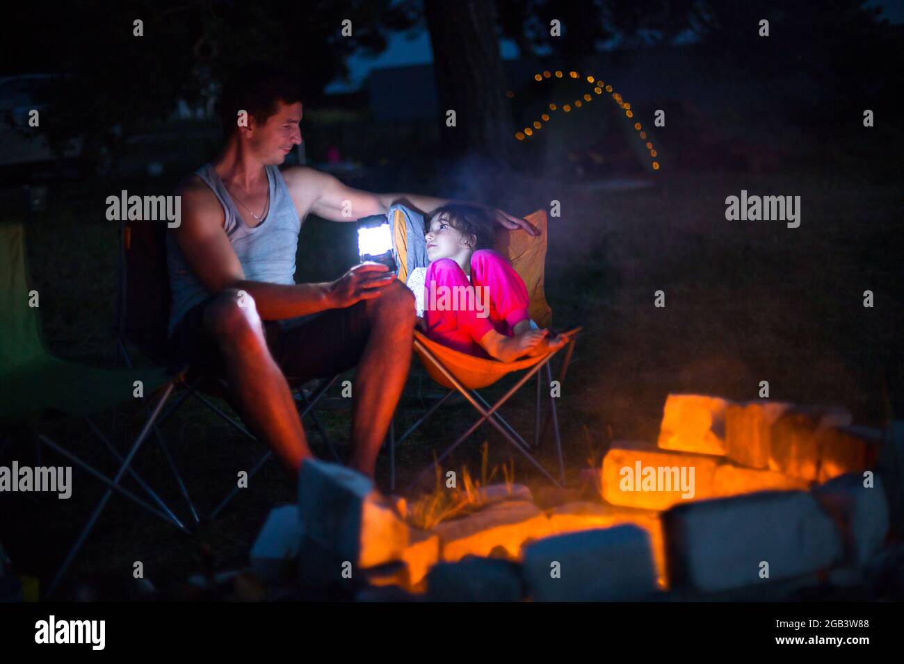 Dad and daughter sit at night by the fire in the open air in the summer